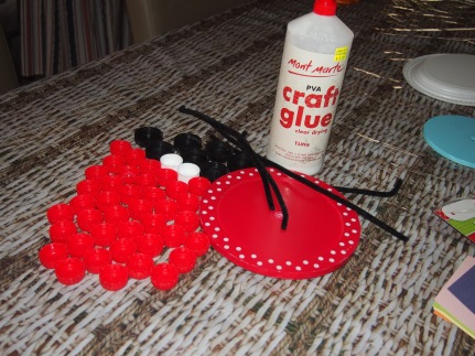Bottle caps of your choice, craft glue, a round piece of card board or plastic, pipe cleaners and goggly eyes
